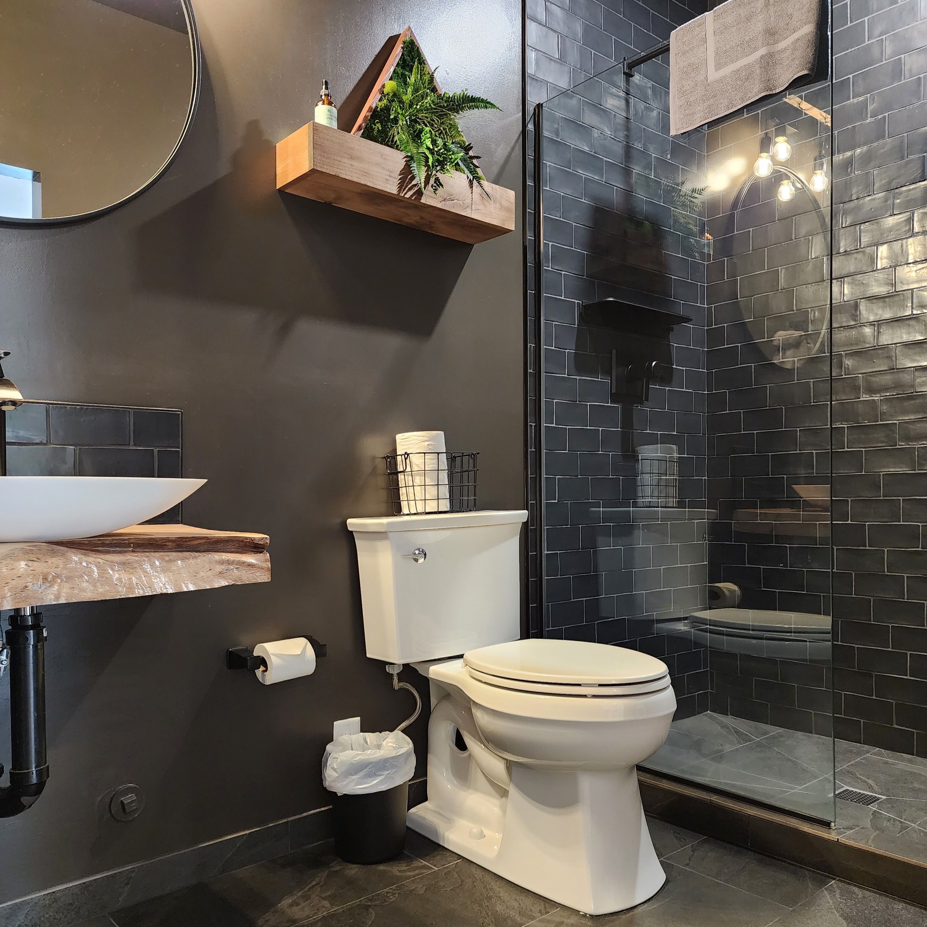 Bathroom in a converted garage suite in Ucluelet, with a live-edge vanity, a wood shelf and a glass shower.