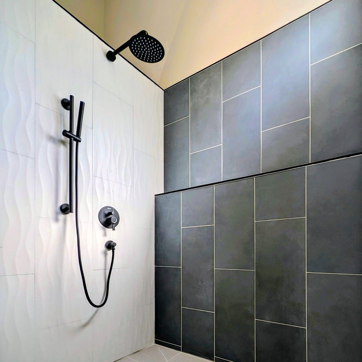 Walk-in shower in Ucluelet with white wave tile, dark wall tile and black fixtures.